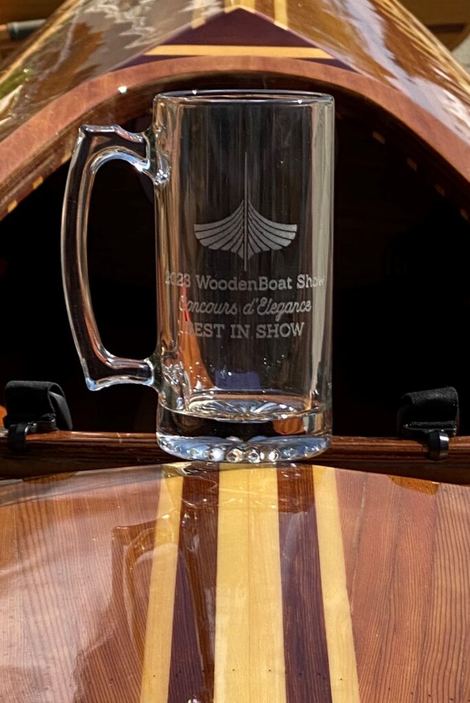 A breathtaking wooden boat with a mug delicately perched atop, showcasing the Newfound Woodworks Cedar Strip Kayak's stunning victory as it wins the prestigious Concours d'Elegance Best