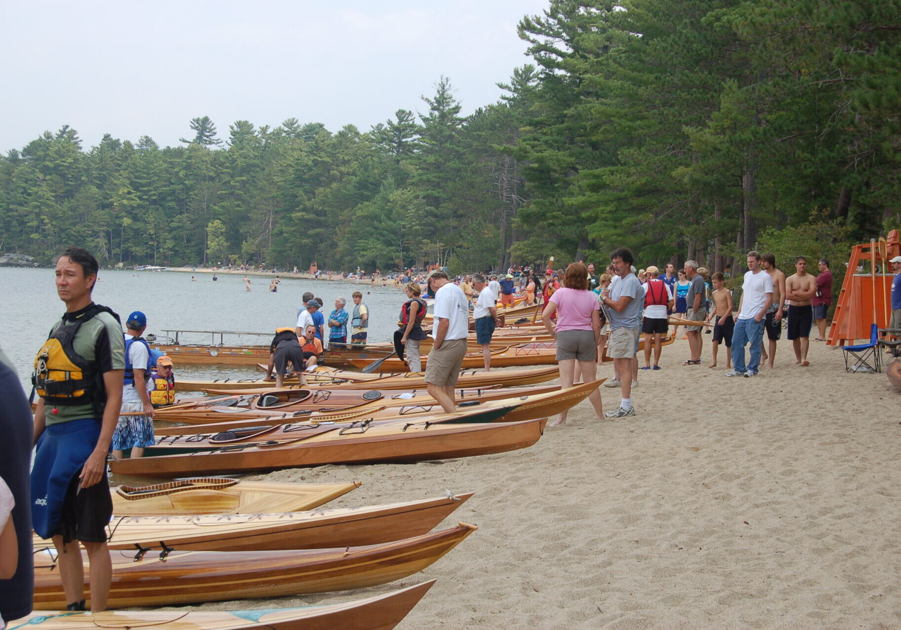 A group of people standing around boats on the beach.