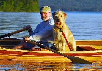 A man and his dog are rowing in the boat.